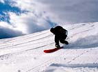 Skieur ou sportif plutot dévalant pente neigeuse/Montagne, on dirait en SKATE; neige ciel bleu parsemé grands nuages blancs. IMAGE SIMPLE mais BELLE ; beauté de la montagne air pur des hauteurs; ciel 